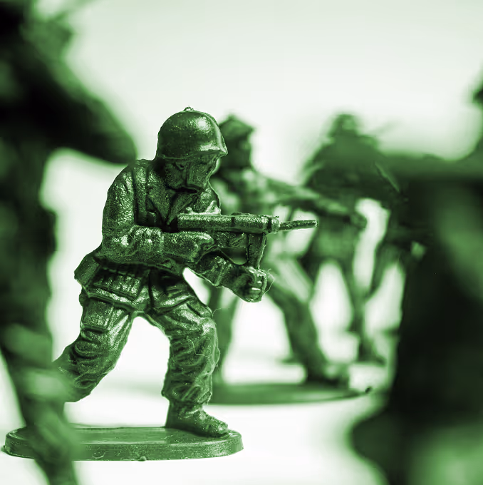 Close-up of green plastic army toy soldier aiming a gun with blurred soldiers in the background. (Saifee Art (unsplash)