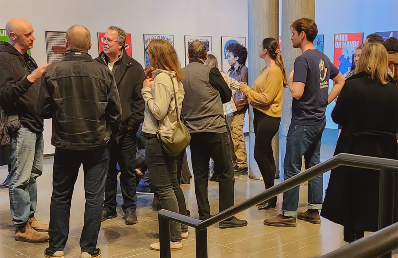 Group of people standing and talking in an art gallery with posters displayed on white walls. (sdgq.ca/marc-h-choko)