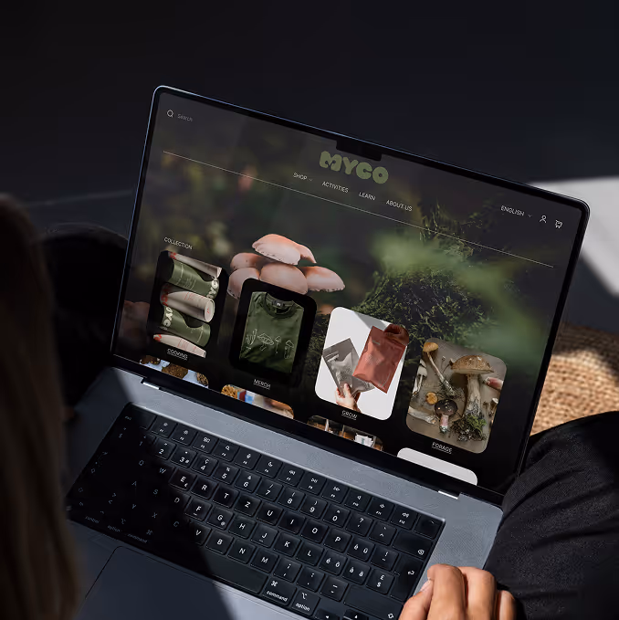 Person viewing a laptop screen with a Myco website showing mushroom-related product collections. (mockup.maison)