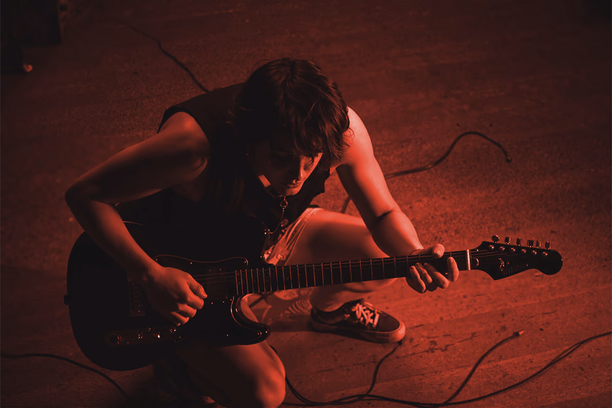Guitarist playing electric guitar on a red-lit stage, caught mid-performance