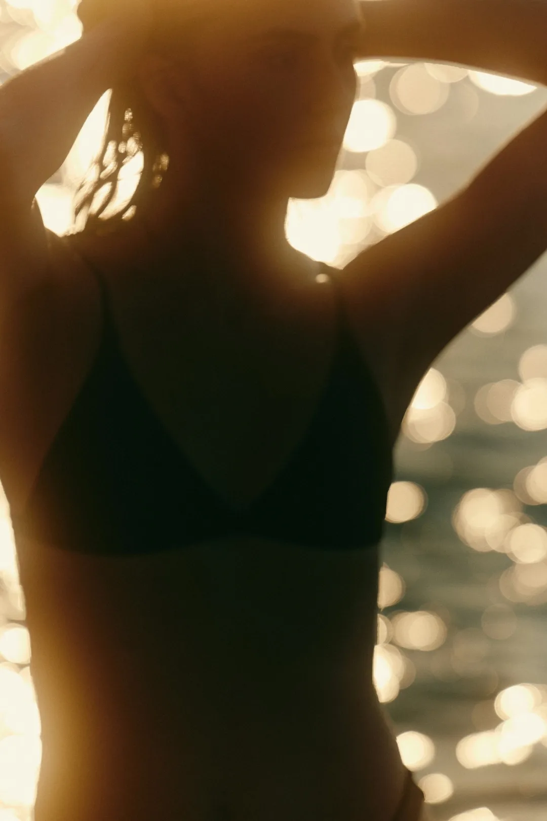 Silhouette of a woman in a bikini with hands on her head against sparkling water light.