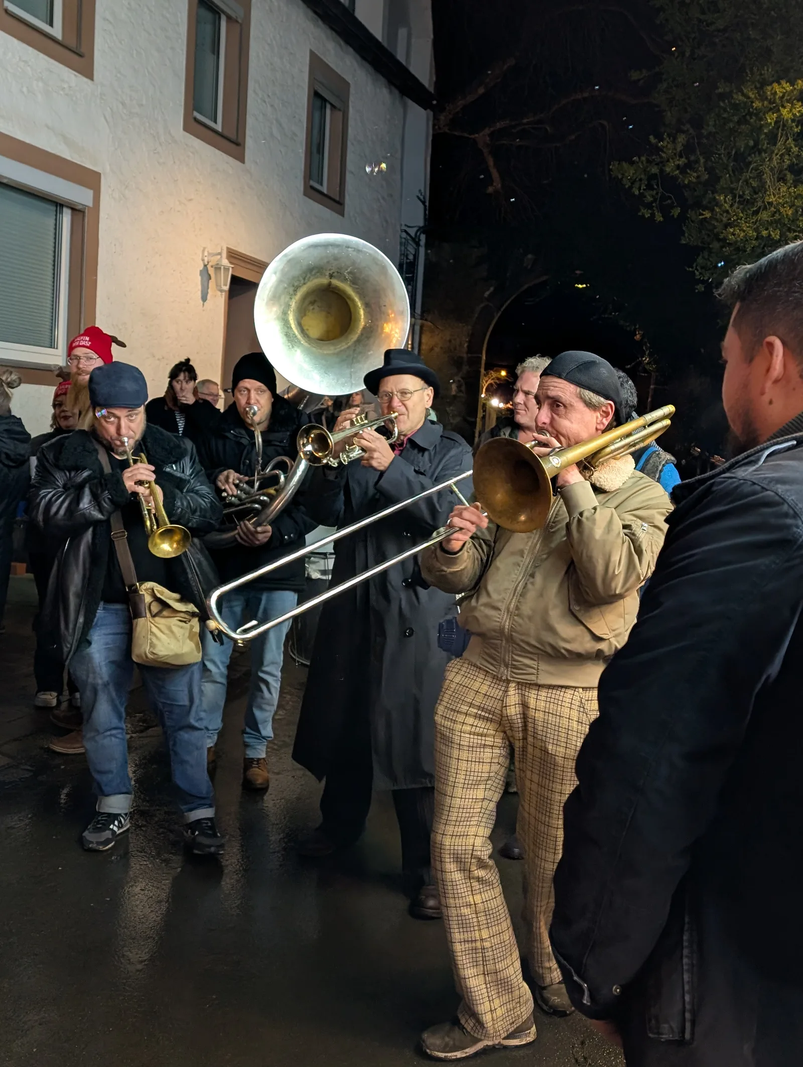 Musikanten spielen Trompete, Posaune und Tuba bei Nacht vor einem weißen Haus.