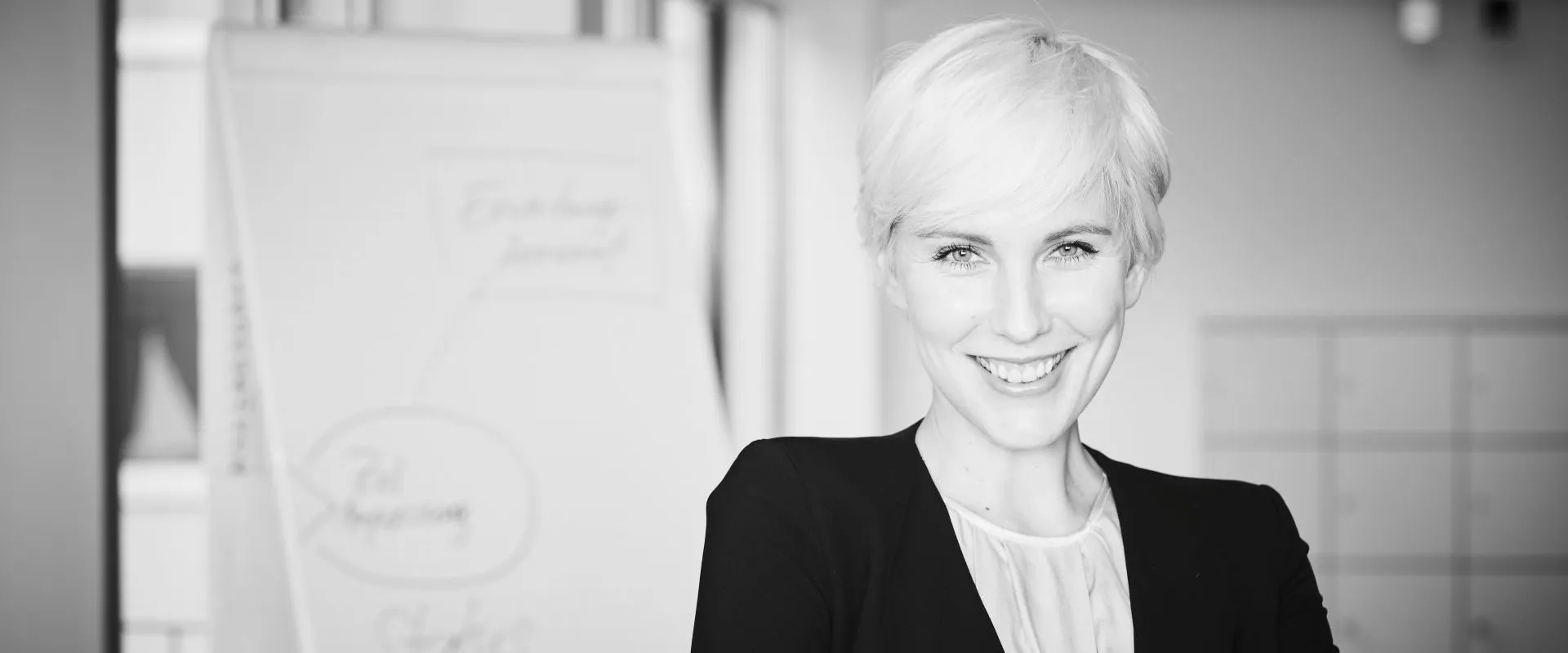 Lächelnde Geschäftsfrau mit kurzen blonden Haaren und verschränkten Armen im Büro