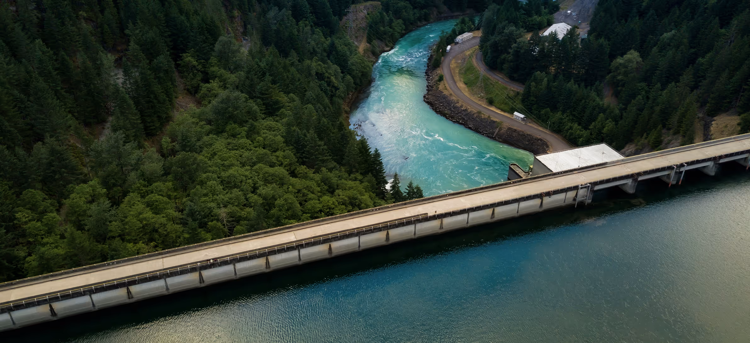 A dam on a river surrounded by dense green forest with clear blue water flowing.