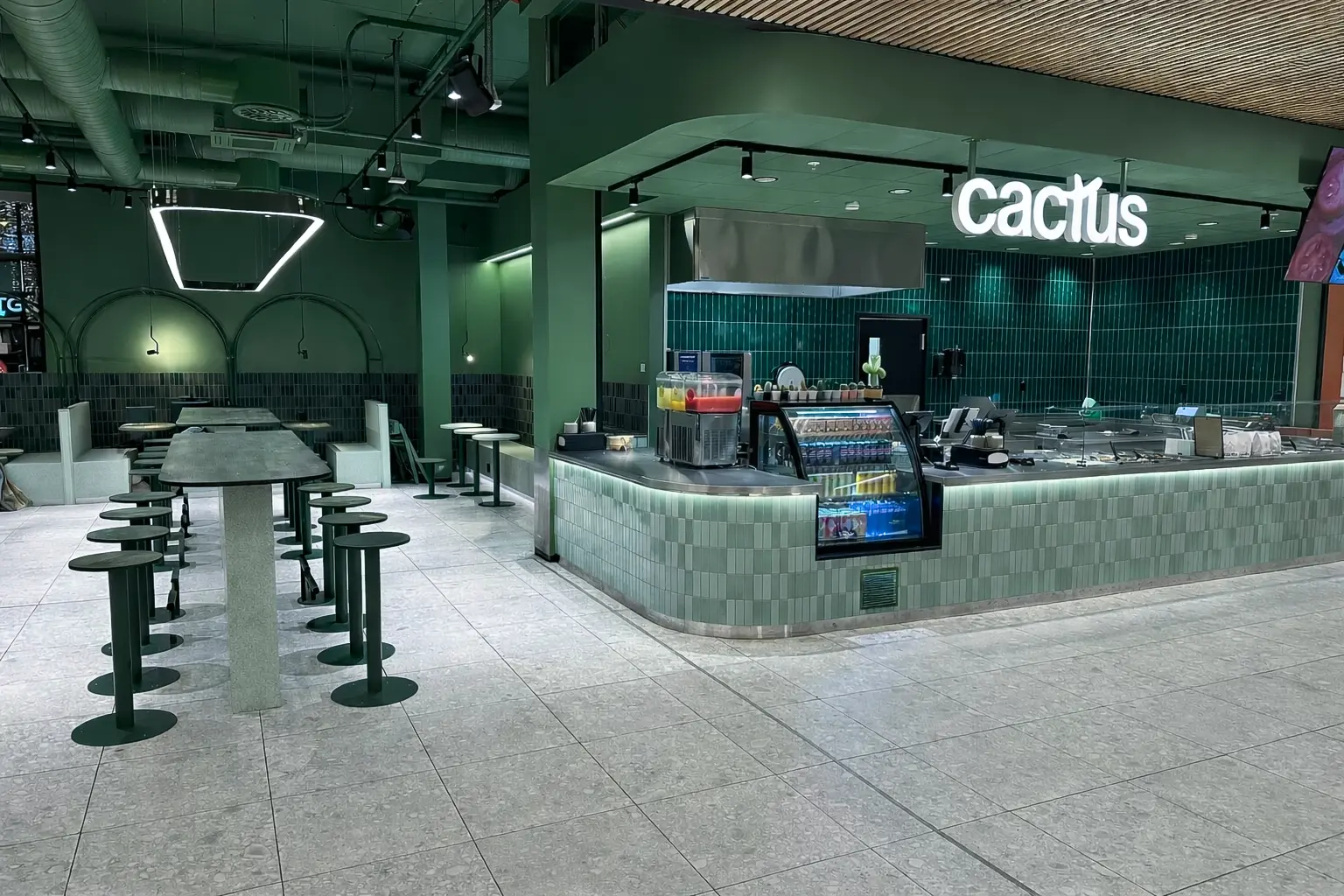 Modern green-themed restaurant interior with high tables, bar stools, and a service counter labeled cactus.