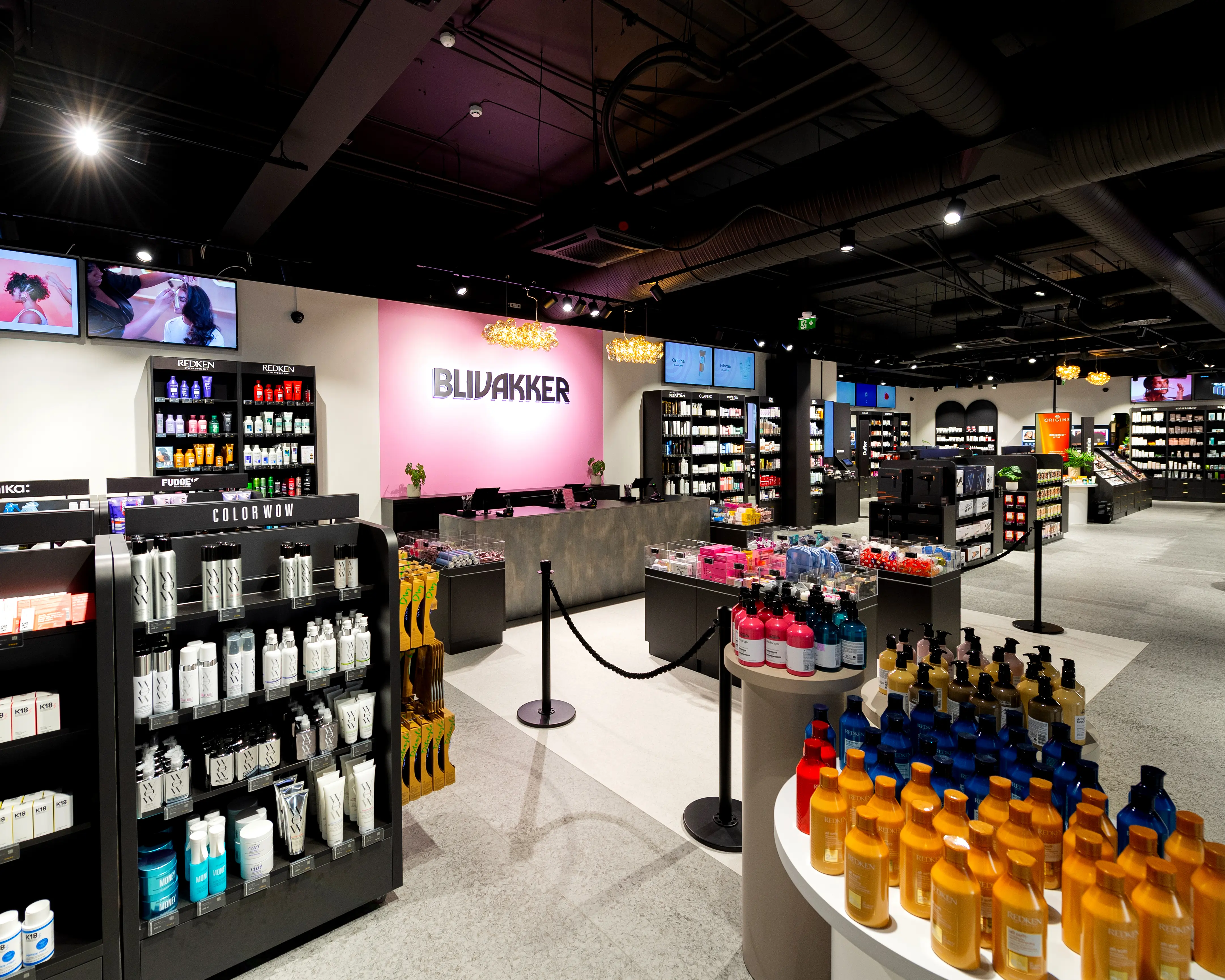 Modern beauty store with shelves of hair care products and a pink wall with 'BLIVAKKER' sign.