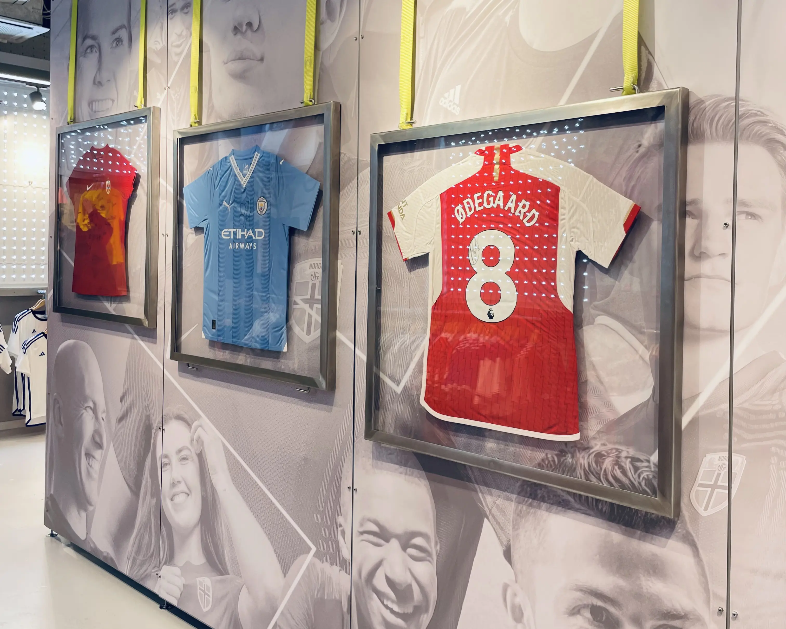 Three framed soccer jerseys hanging on a wall with black and white portraits in the background.