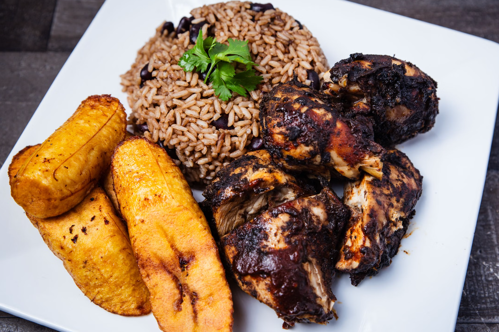 A plate of golden Caribbean fried chicken served with rice, beans, and fried plantains — similar to Dominican pica pollo served at local street spots.