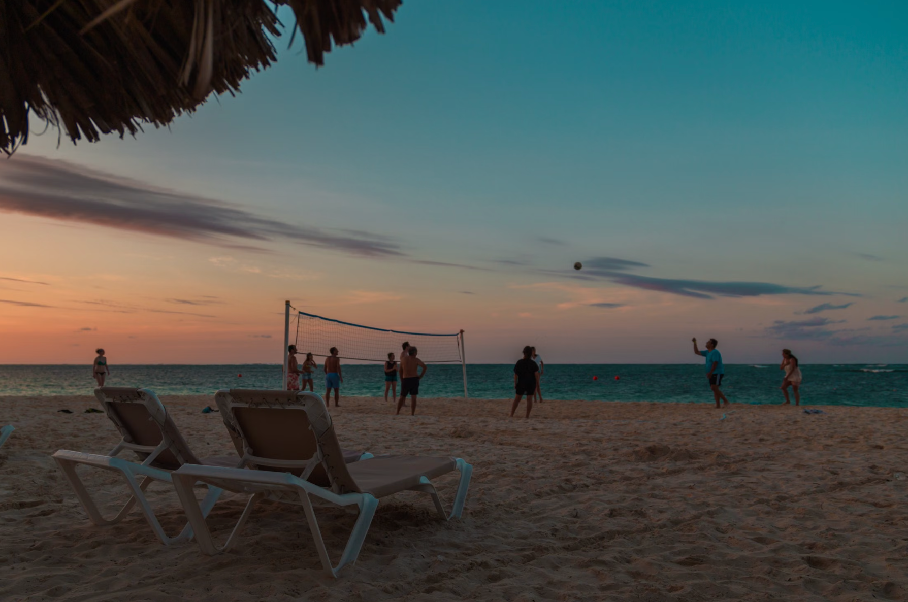 Sun loungers on a white sand all-inclusive resort beach at Bávaro, Punta Cana, on the Dominican Republic east coast evening people playing in beach.
