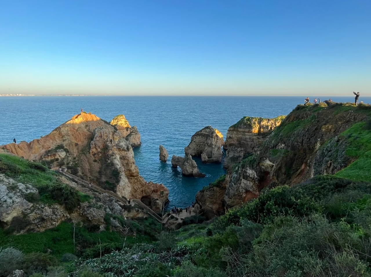 Golden limestone rock stacks and natural arches at Ponta da Piedade headland Lagos Portugal at sunset with visitors on the cliffs.