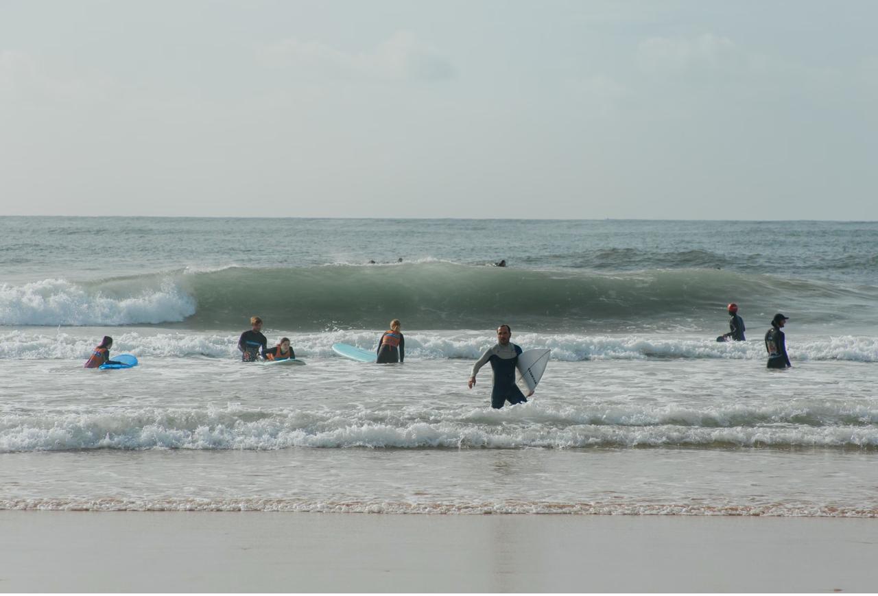 A group of beginner surfers in wetsuits with boards in the Atlantic waves during a surf lesson on the Algarve coast Portugal.