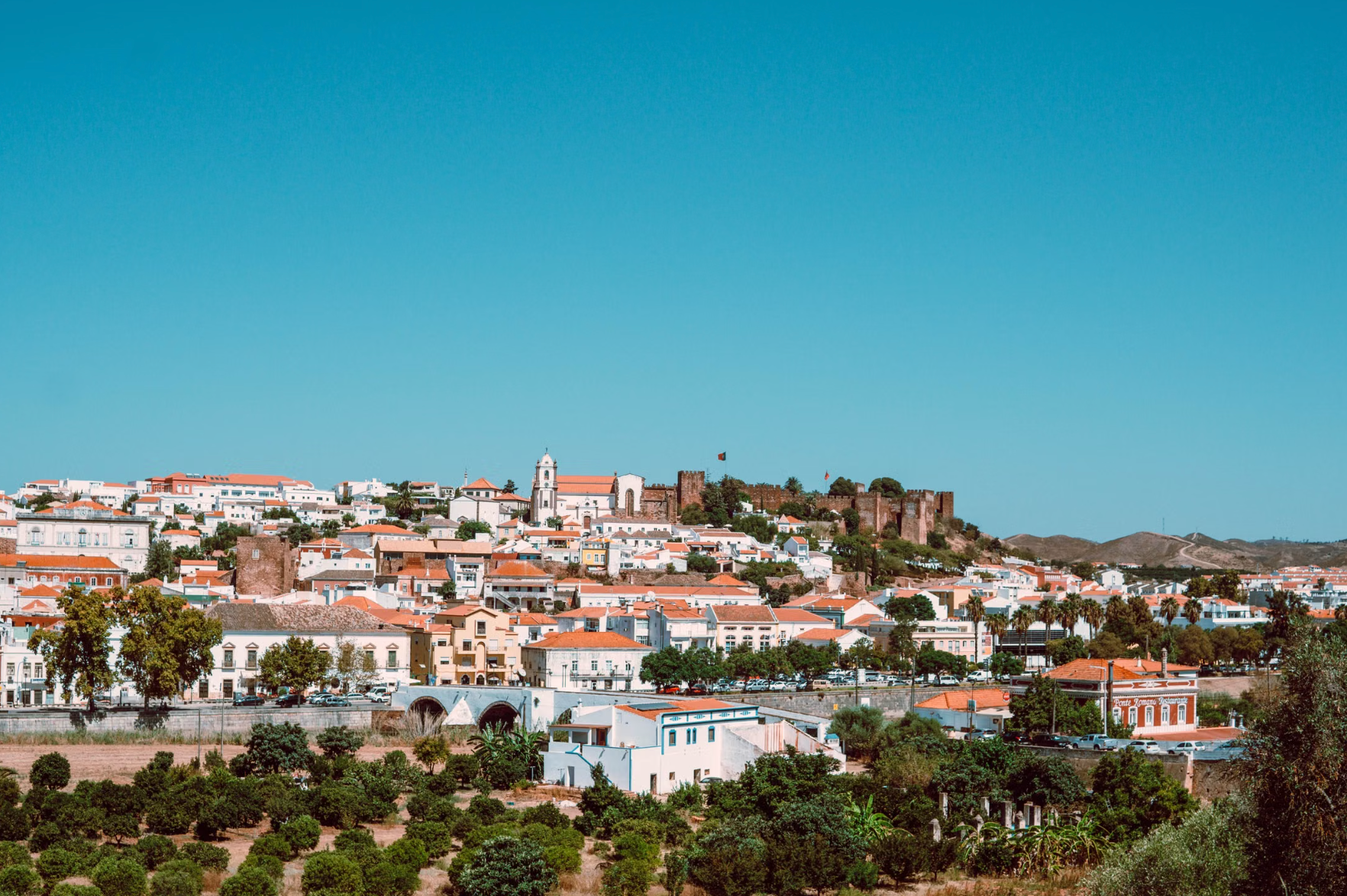 Aerial view of Silves town with white and terracotta buildings orange groves and the red Moorish castle walls on the hill Algarve Portugal.