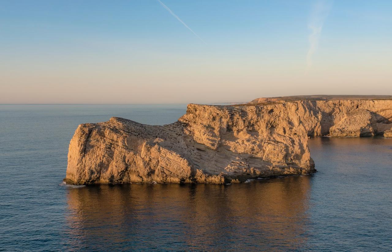 A large flat limestone cliff rising from the Atlantic Ocean at golden hour near Sagres at the southwestern tip of Portugal.