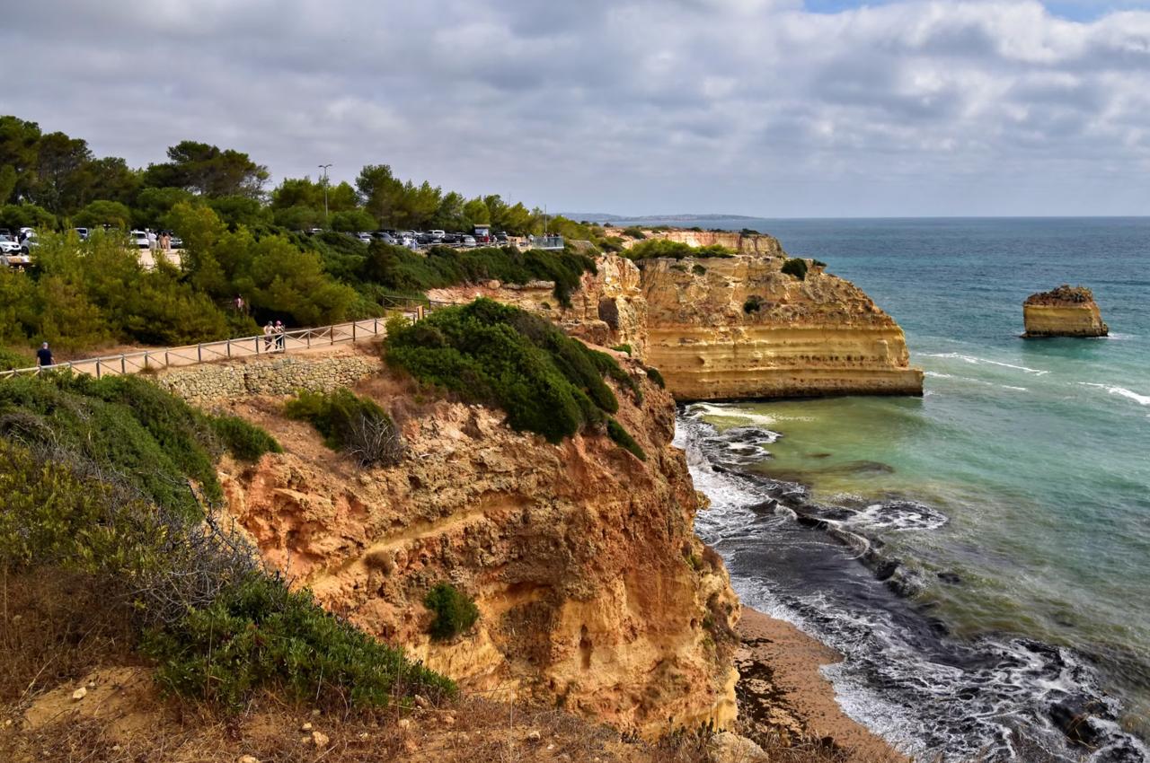 Wooden boardwalk clifftop trail along golden sandstone cliffs above turquoise Atlantic water on the Seven Hanging Valleys route Algarve Portugal.