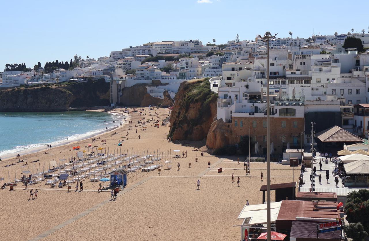 Albufeira beach with rows of sun loungers white buildings stacked on the cliff and the Atlantic coastline stretching into the distance Algarve Portugal.