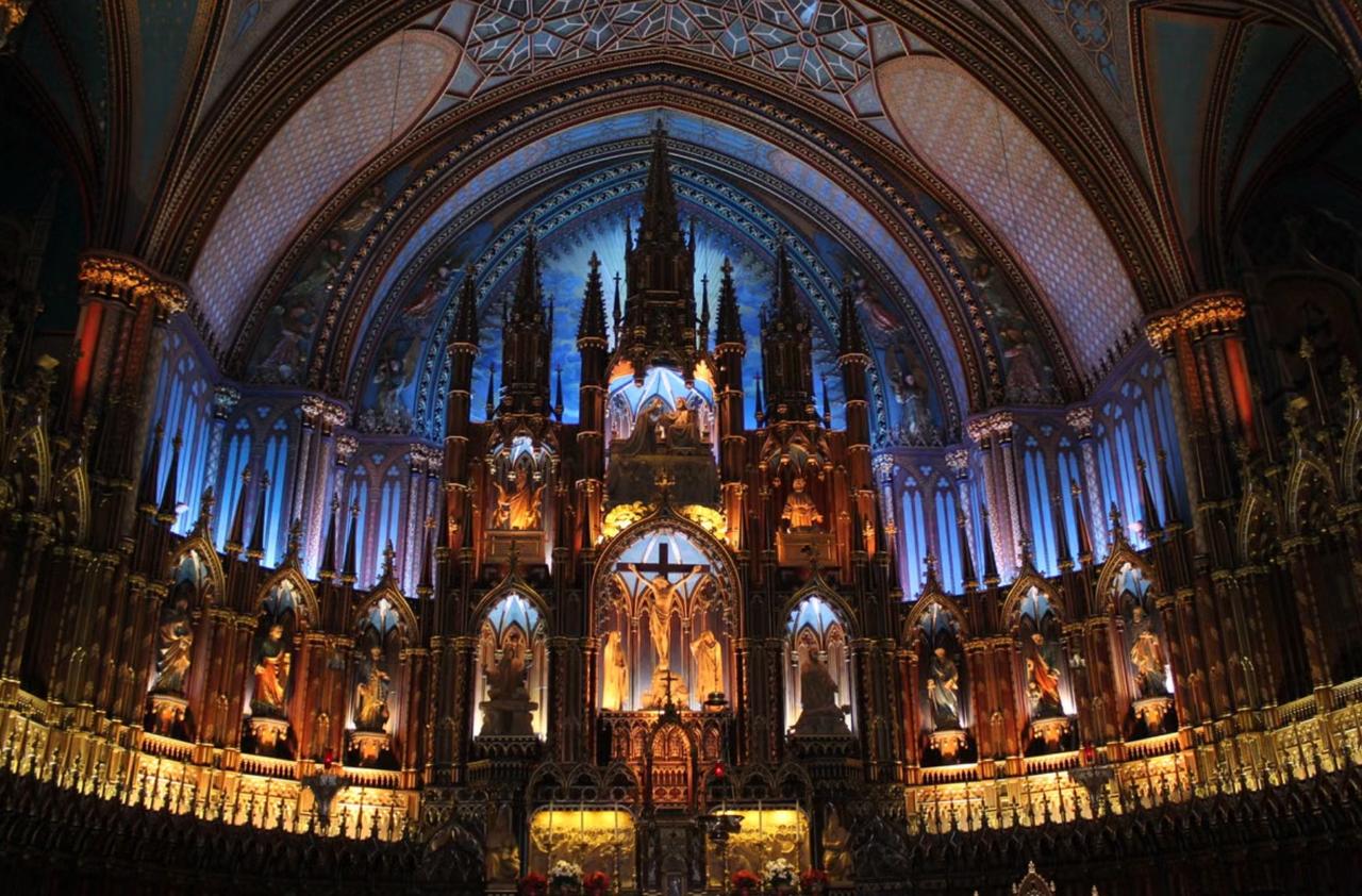 Interior of Notre-Dame Basilica in Montreal, its blue-and-gold vaulted ceiling and ornate gilded altar lit up after dark.