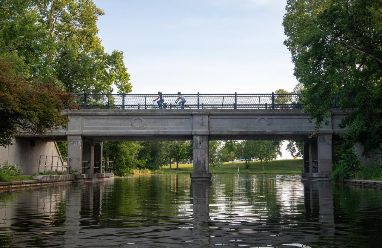 Cyclists riding the paved path alongside the Lachine Canal with former industrial buildings in the background
