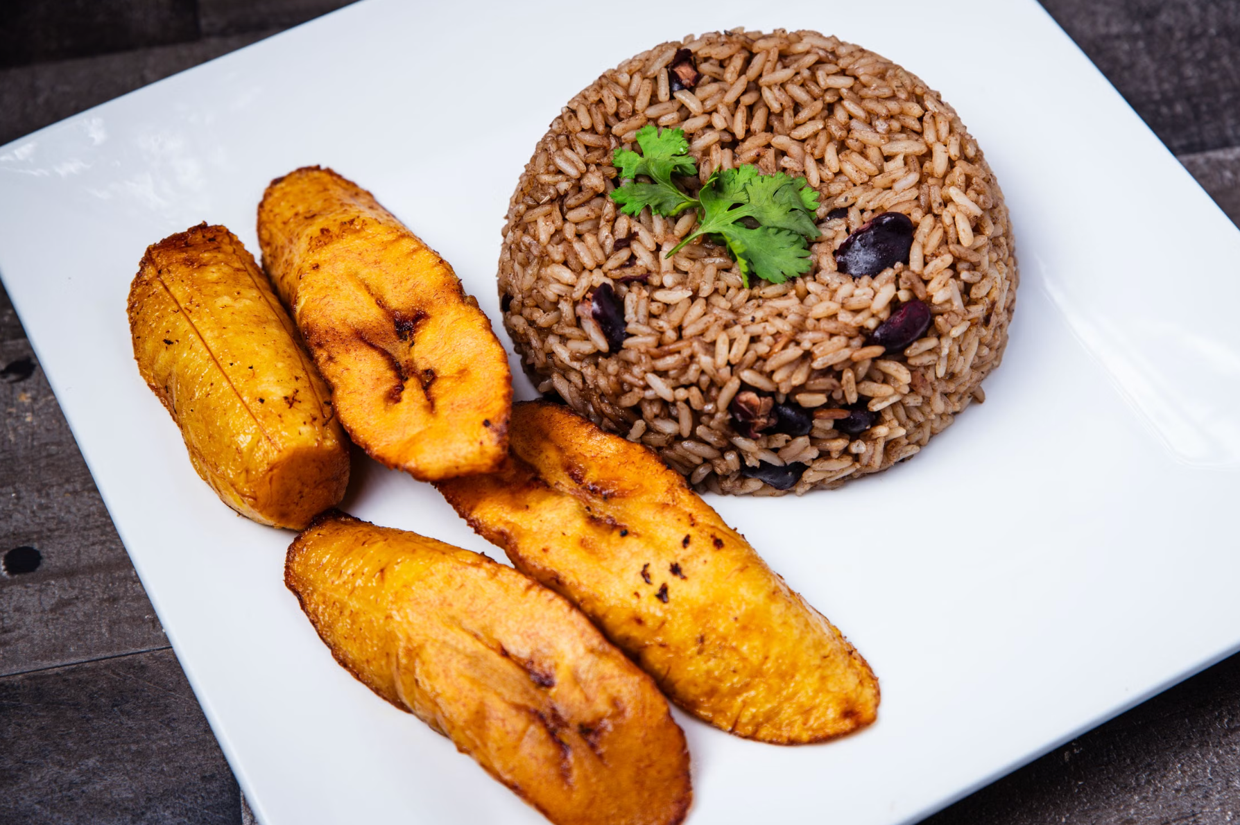 white plate of Dominican-style rice and red beans (moro) with four pieces of fried sweet plantain (maduros).