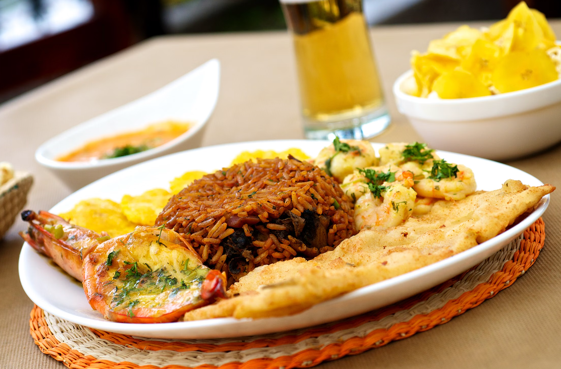 Dominican seafood platter with a grilled garlic prawn, sauteed shrimp, savory moro rice, a fried fish fillet and tostones, served with a side of plantain chips and a cold beer.