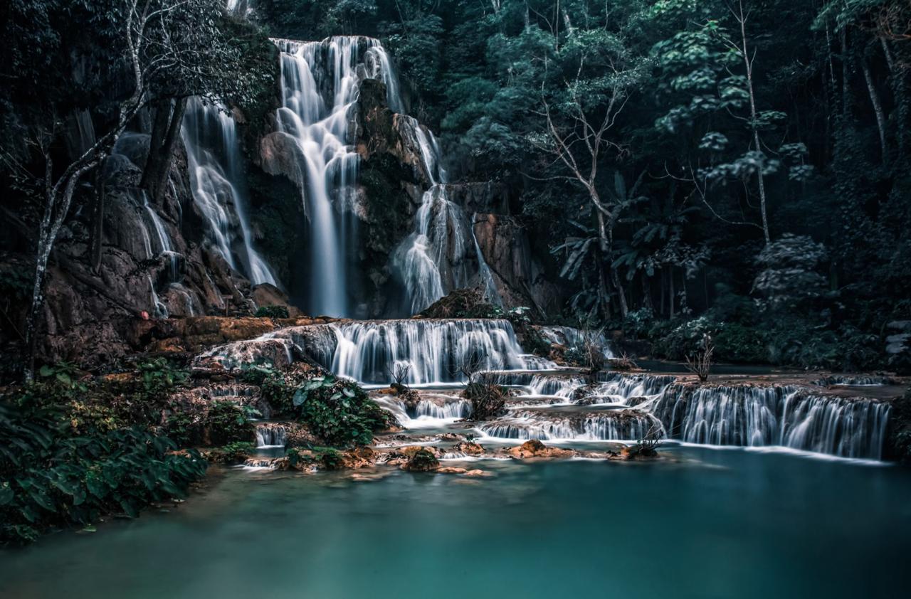 Cascading waterfall flows into emerald pool surrounded jungle vegetation