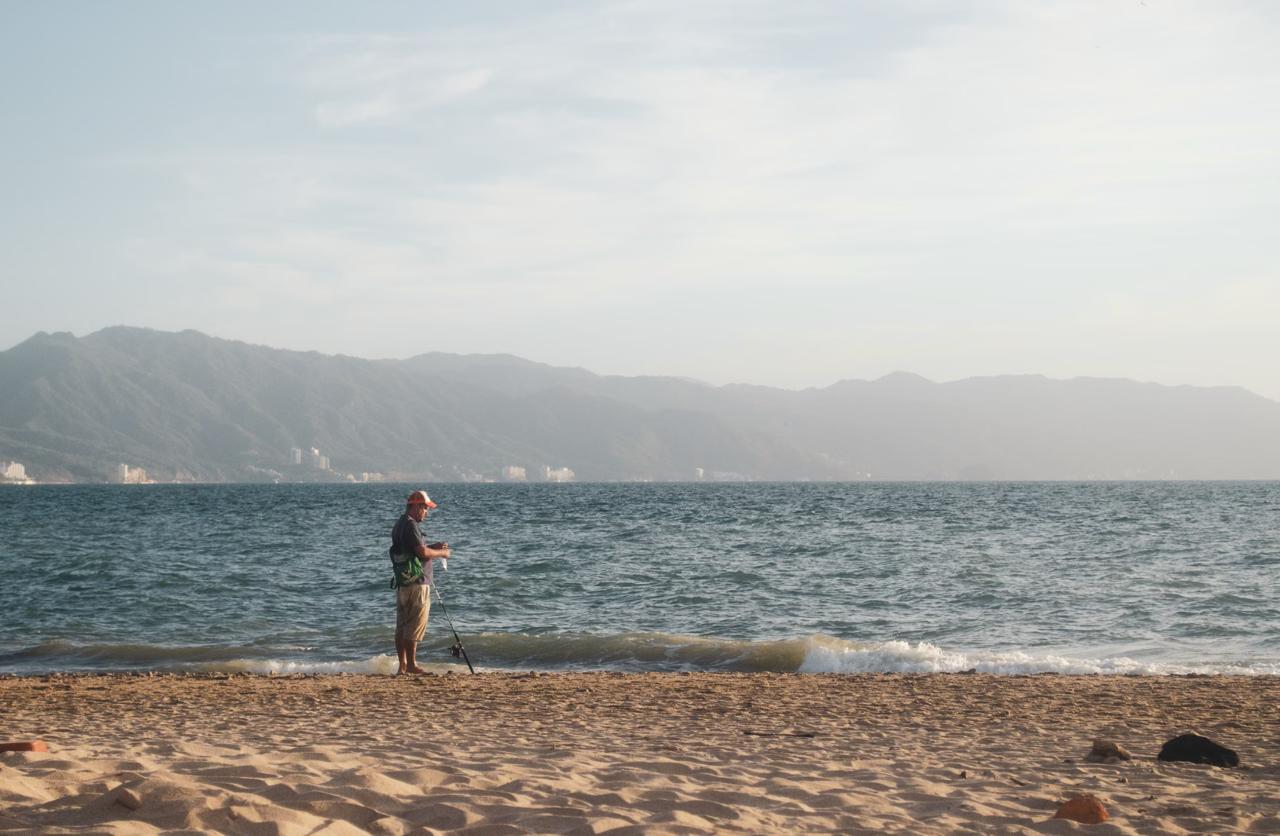 The calm, glassy turquoise shallows of the Sea of Cortez near La Paz, with a bare desert headland and a distant kayak.