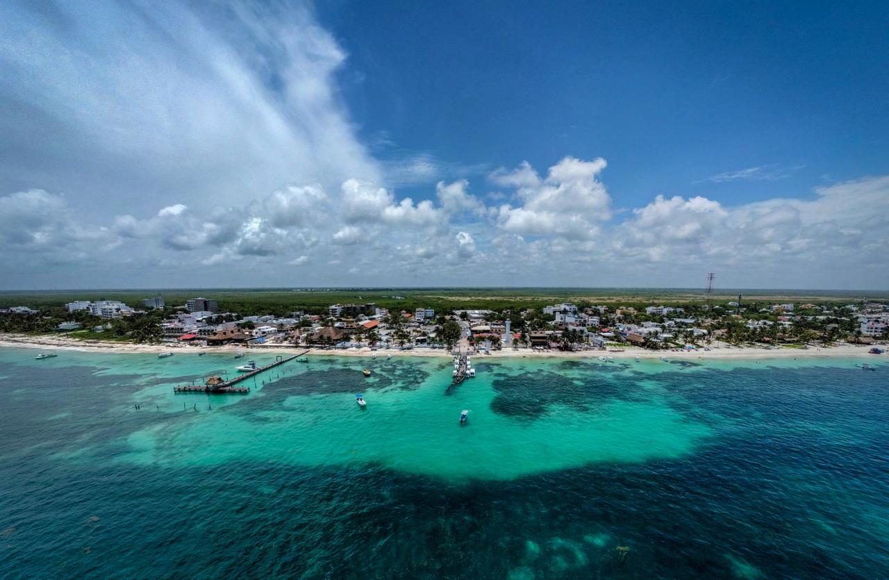 Aerial of the Puerto Morelos fishing village with its leaning lighthouse, wooden piers and boats over the turquoise reef lagoon.