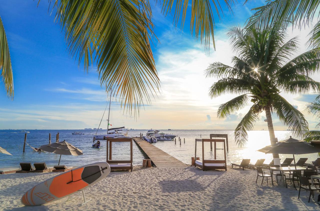 Palm-lined white-sand beach on Mexico's Caribbean coast with calm turquoise water and a few beach umbrellas