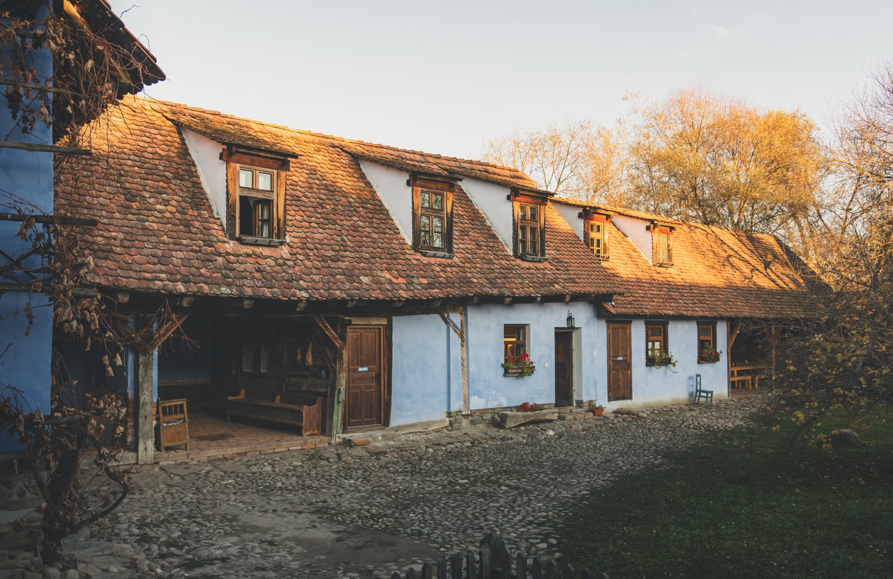 Thatched-roof farmhouse and tall wooden church among trees at the Dimitrie Gusti National Village Museum