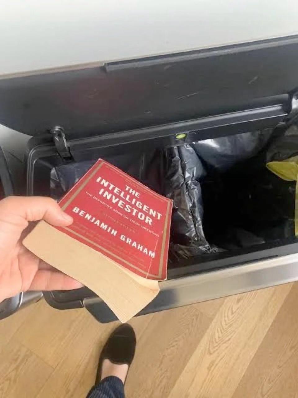 Hand dropping Benjamin Graham book The Intelligent Investor into a trash can.