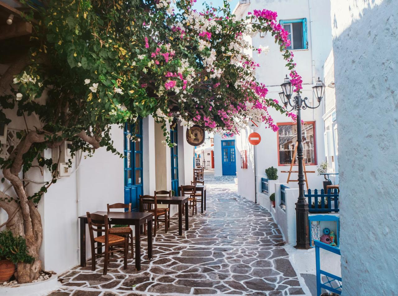 A narrow cobblestone alley in Plaka lined with pink bougainvillaea, taverna tables, and neoclassical facades.