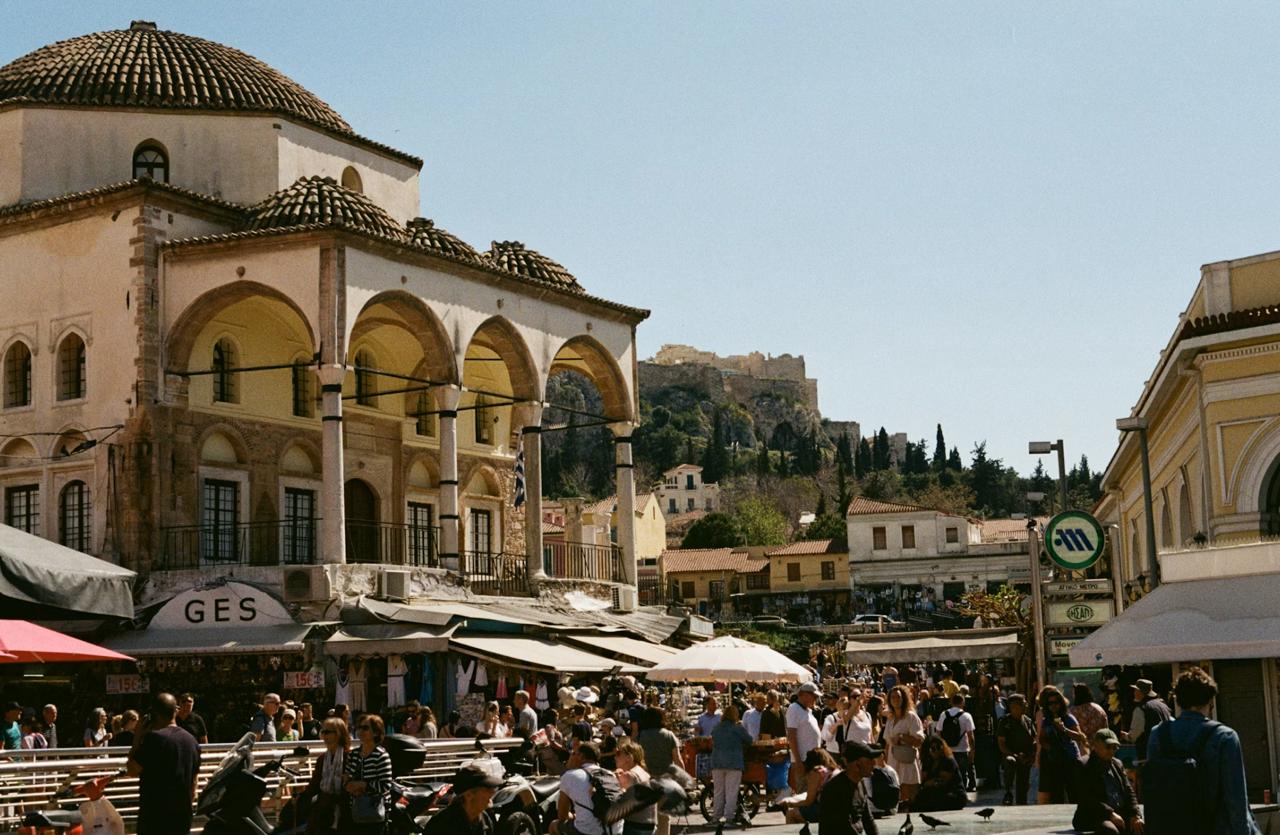 Monastiraki Square at dusk crowded with vendors, restaurants, and shoppers walking.