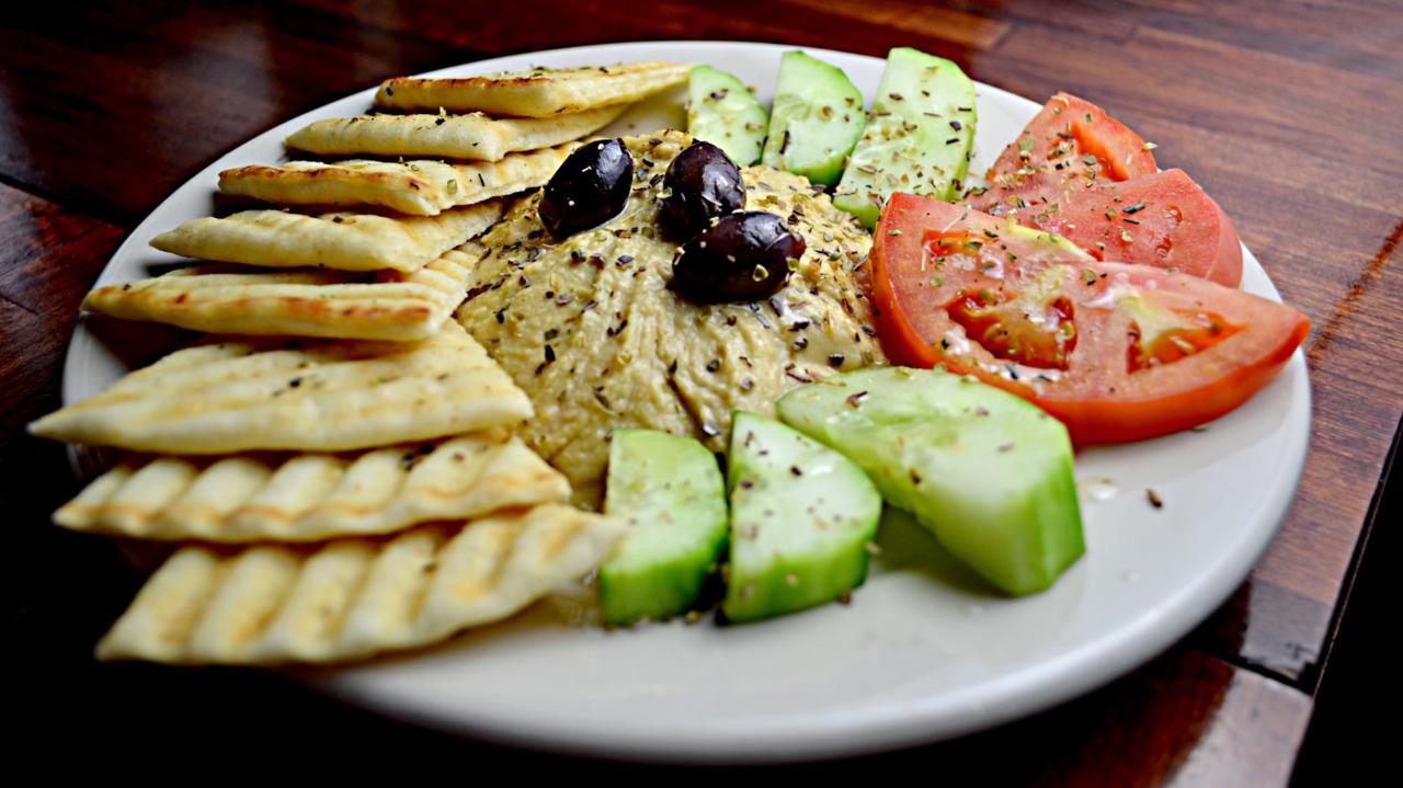 A wooden taverna table spread with souvlaki skewers, Greek salad, tzatziki, and a carafe of white wine.