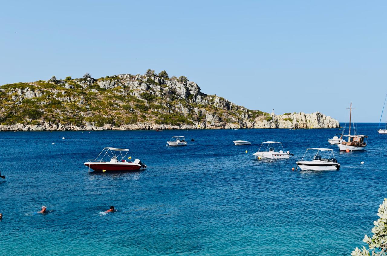 Swimmers in the turquoise thermal water of Lake Vouliagmeni beneath its rocky cliff.