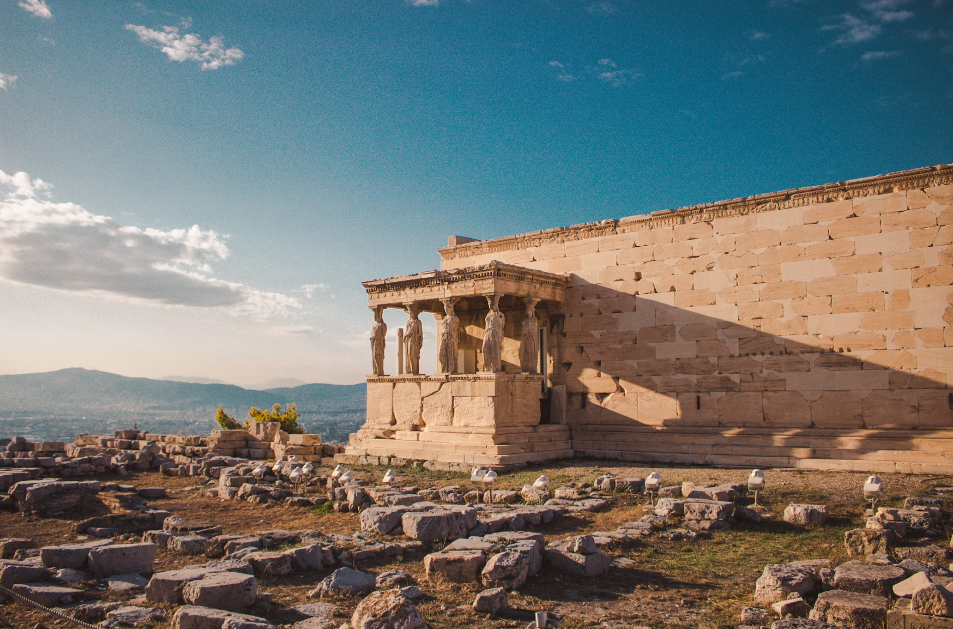 Temple of Hephaestus with intact marble columns surrounded by ruins and green vegetation.