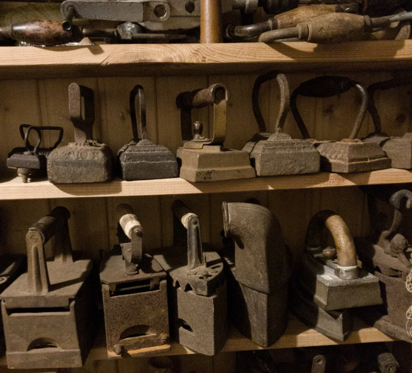 Antique cast-iron flat irons displayed on wooden museum shelves