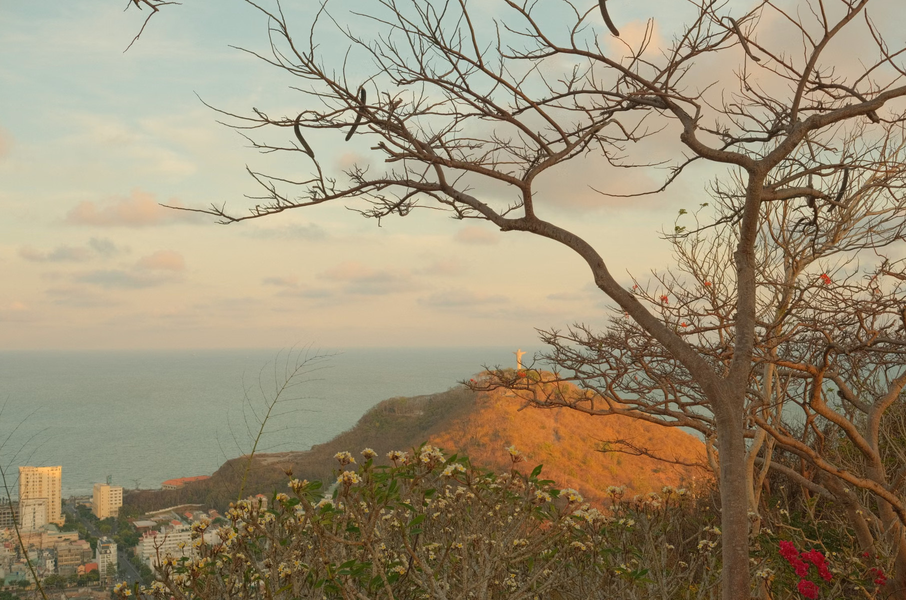 Hilltop Christ statue overlooking coastline and city at sunset