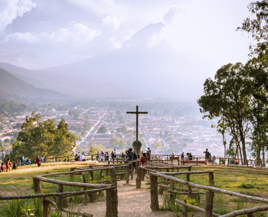 Hilltop cross viewpoint overlooking a valley town at sunset