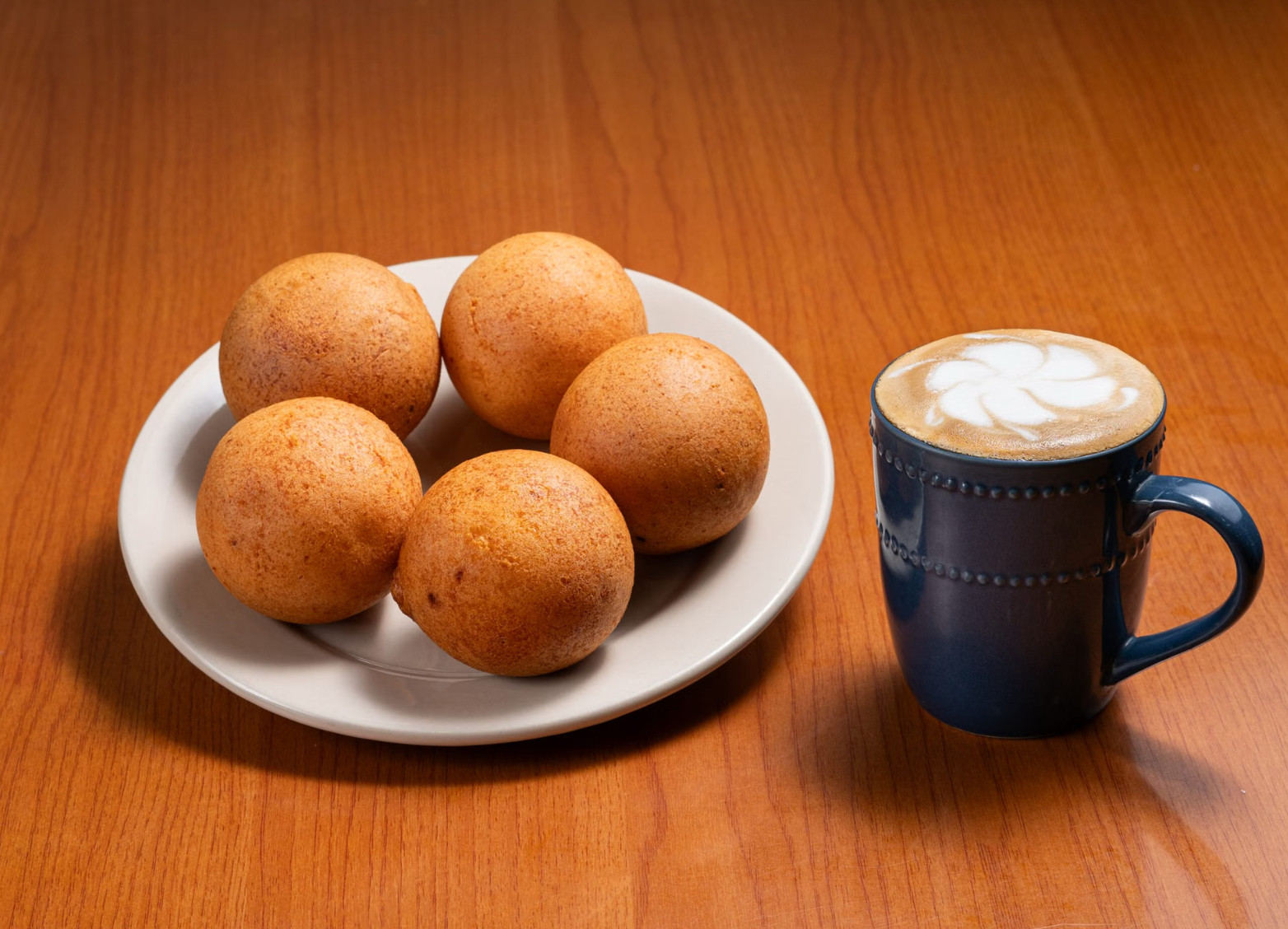 Colombian buñuelos on a plate beside a frothy coffee