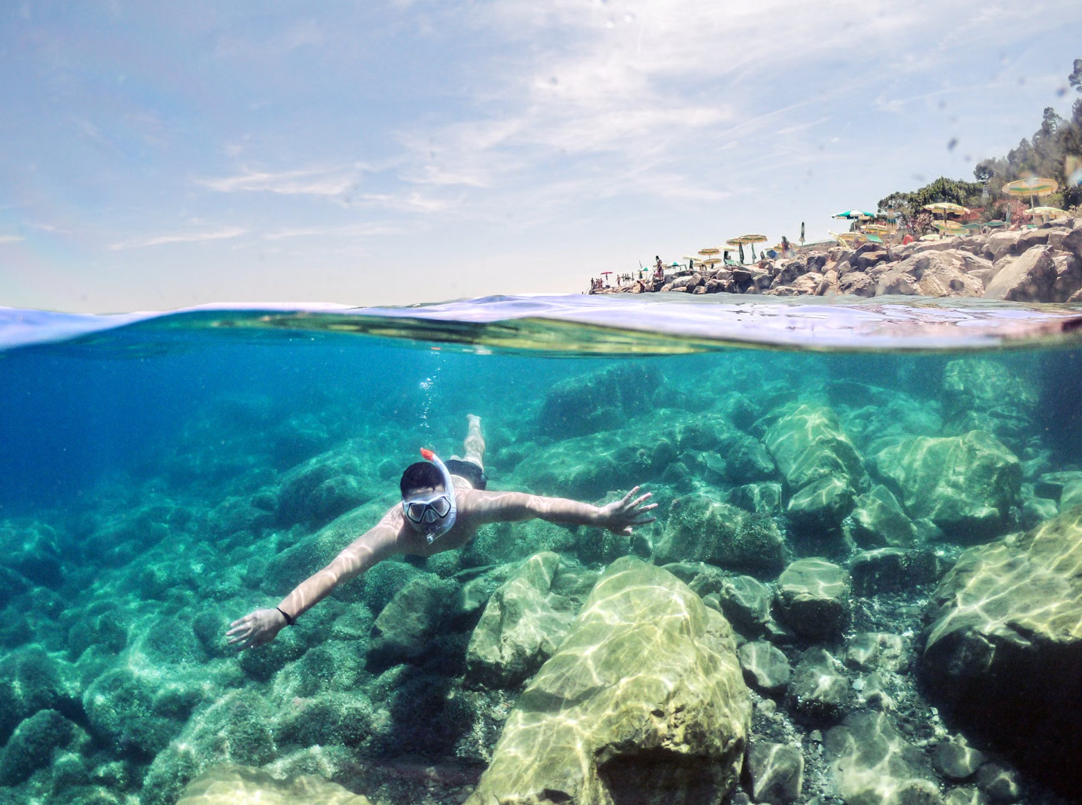 Snorkeler swimming over rocks in clear turquoise coastal water