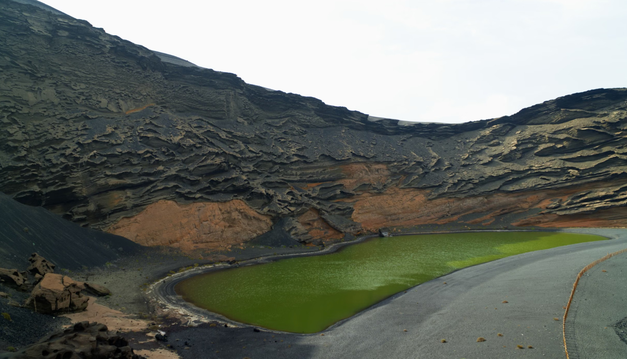 Green volcanic crater lake surrounded by dark lava cliffs