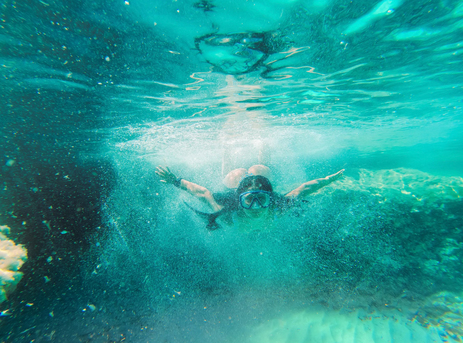 Person snorkeling underwater through bubbles in clear green sea