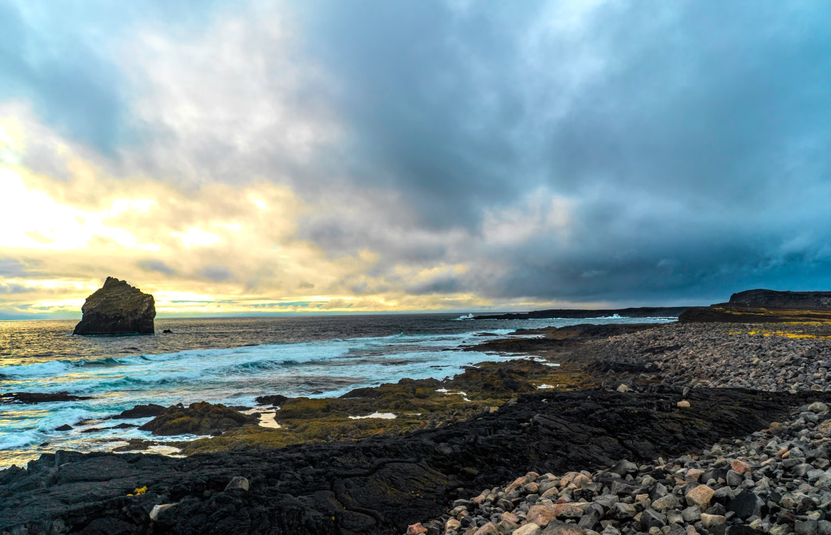Rugged rocky coastline with sea stack under cloudy sunset sky