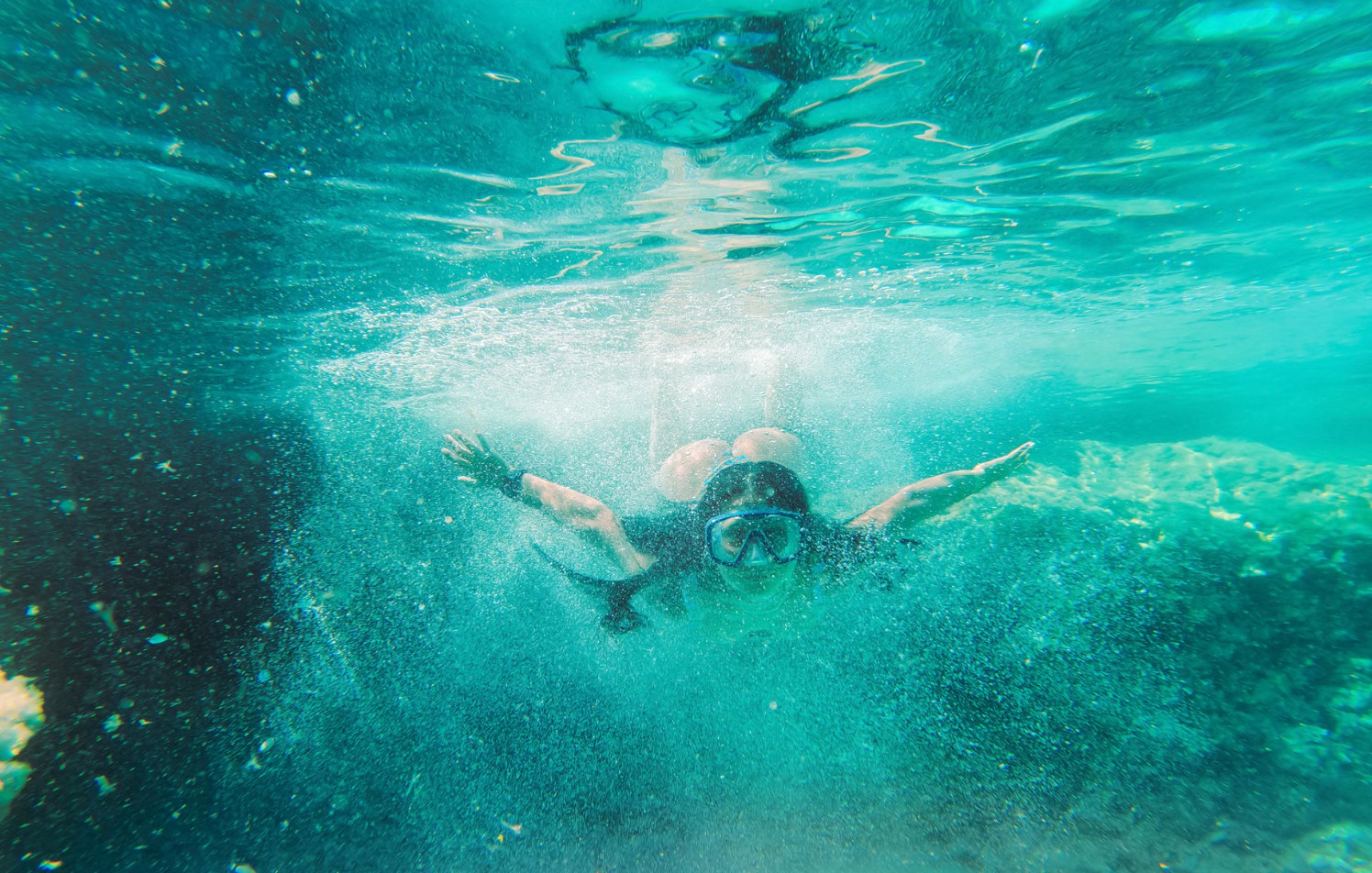Snorkeler in mask diving underwater through clear turquoise water