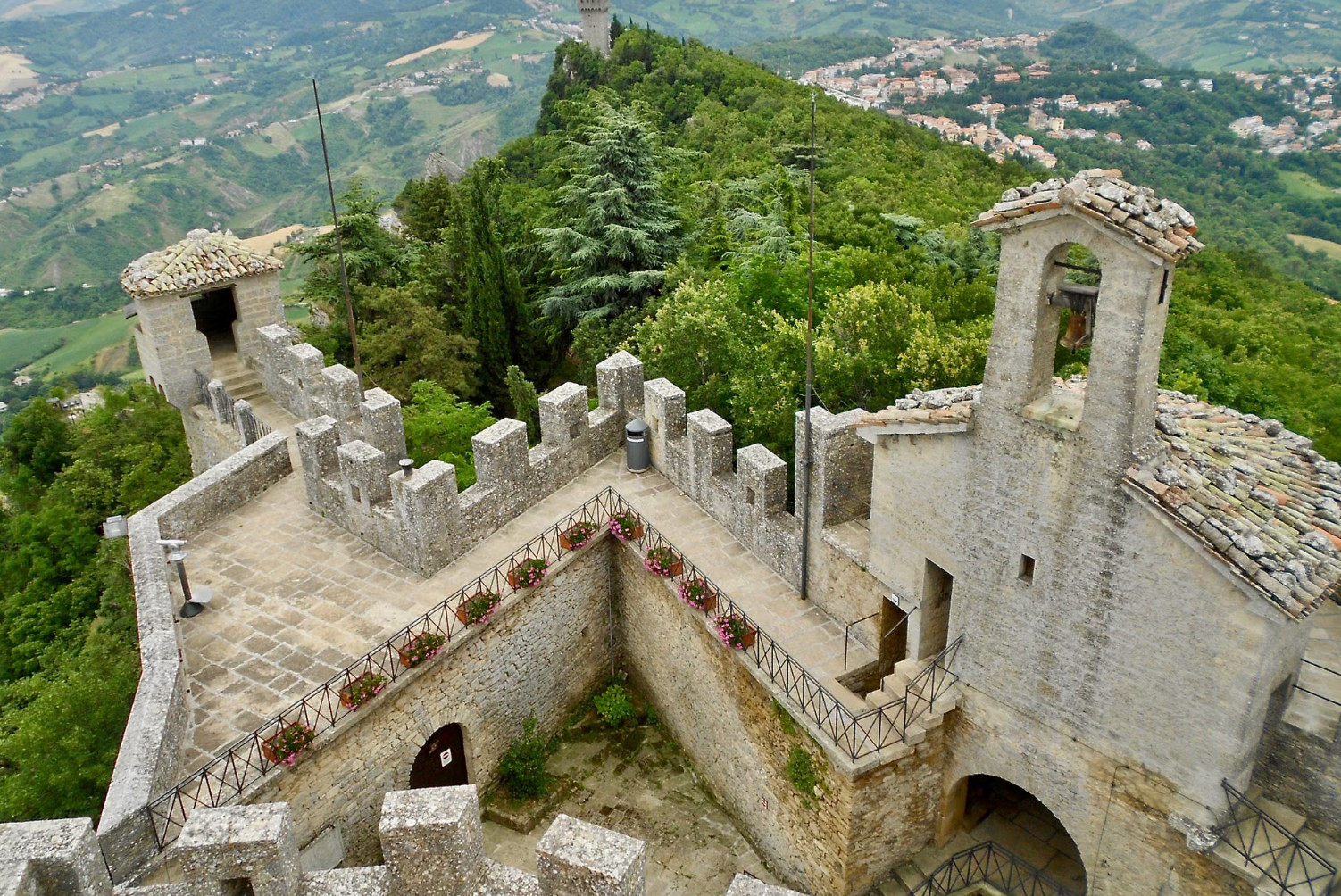 Tower view over San Marino battlements and wooded ridge.