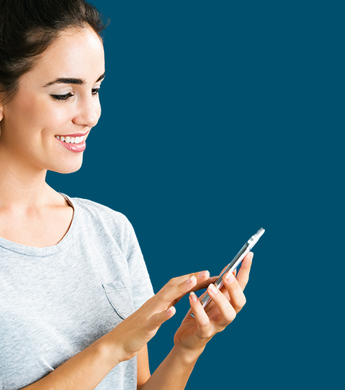 Smiling woman in a gray shirt looking at and using a smartphone against a blue background.