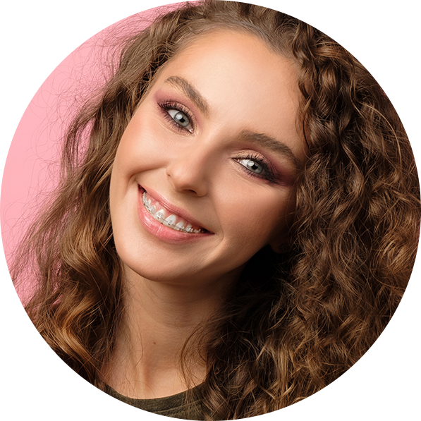 Smiling woman with curly brown hair and braces on teeth against a pink background.