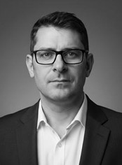 Photo of Ian Pillay wearing glasses and a suit jacket over a white shirt.