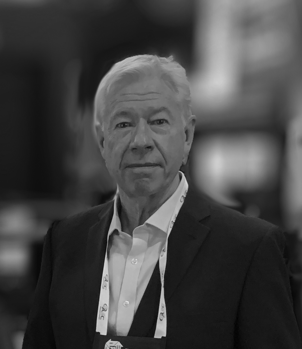 Photo of Keith Downes wearing a suit and conference badge in a blurred background.