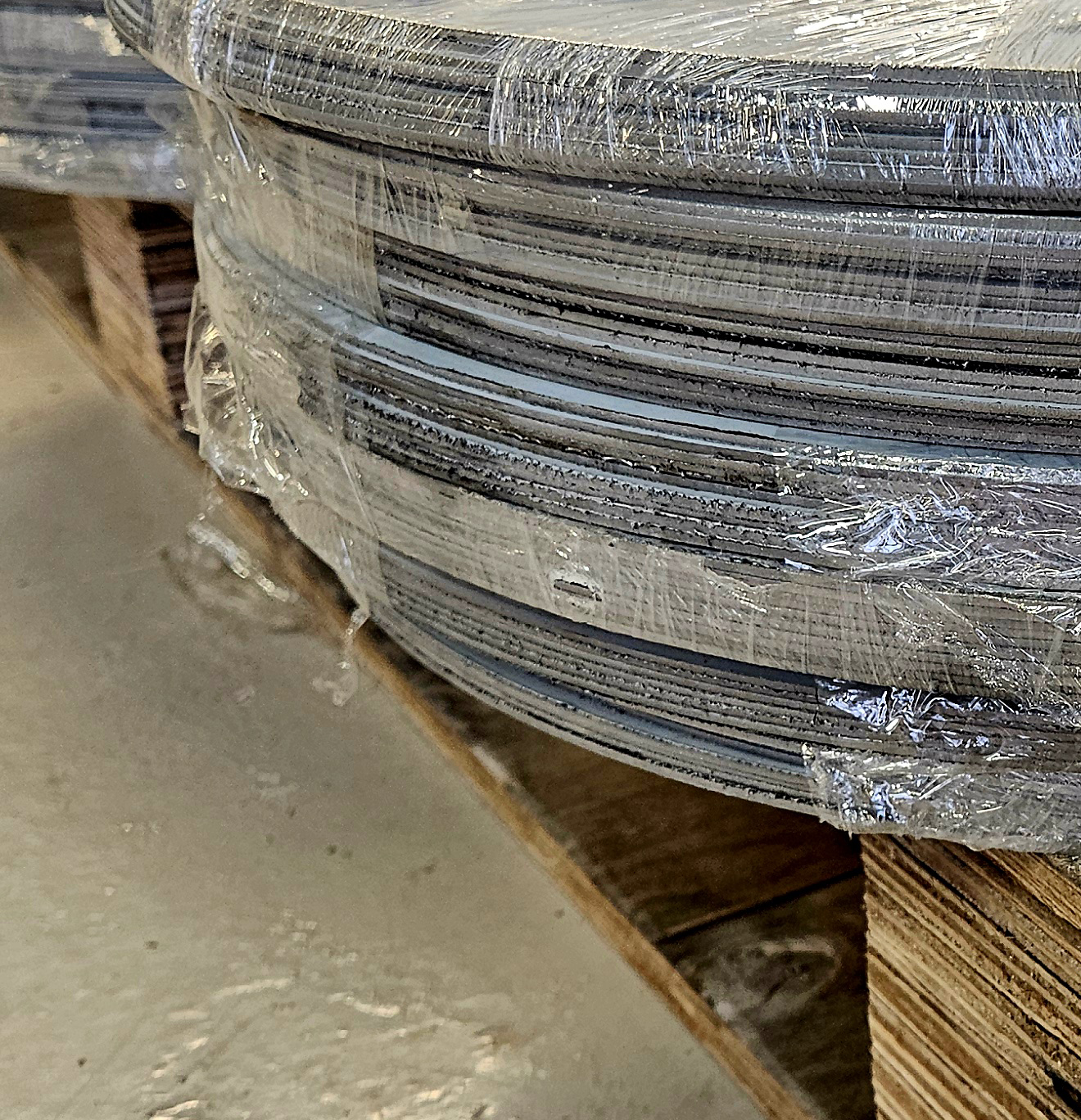 Close-up of large metal coils wrapped in plastic on a wooden pallet in a warehouse.