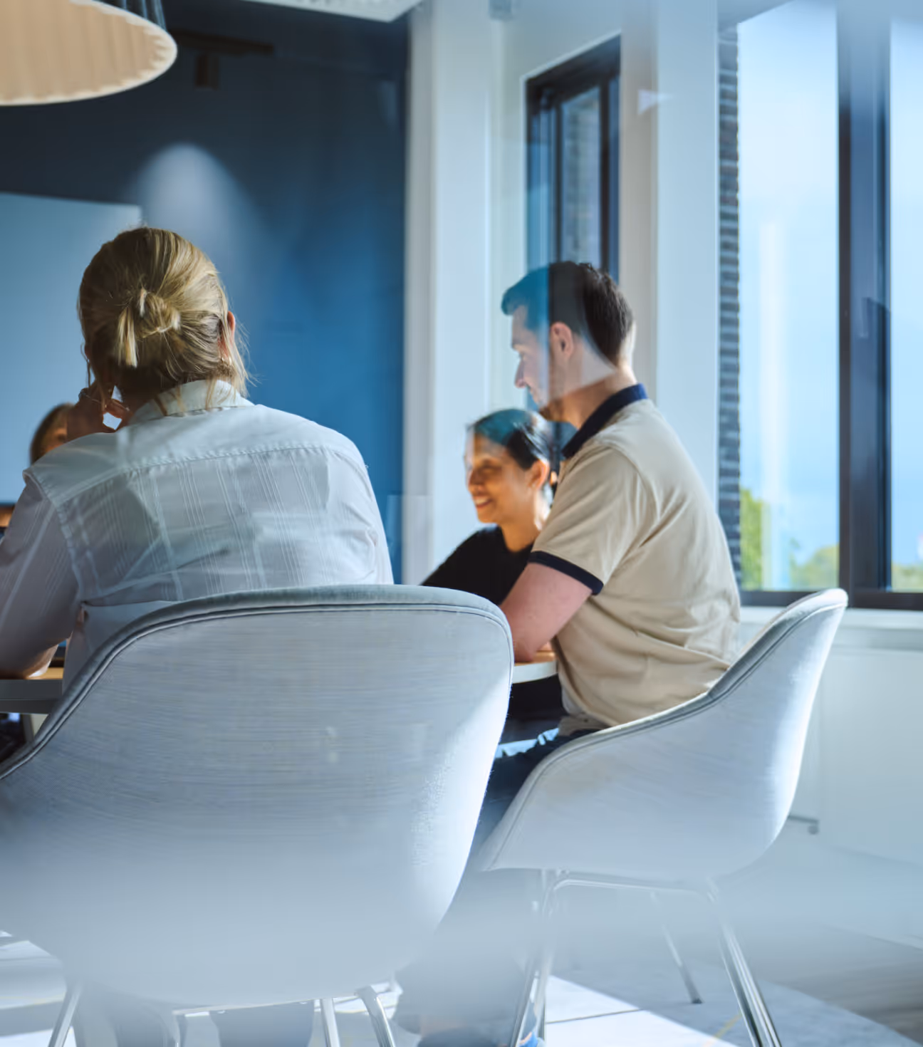 Three people sitting on gray chairs around a table in a bright modern office space.